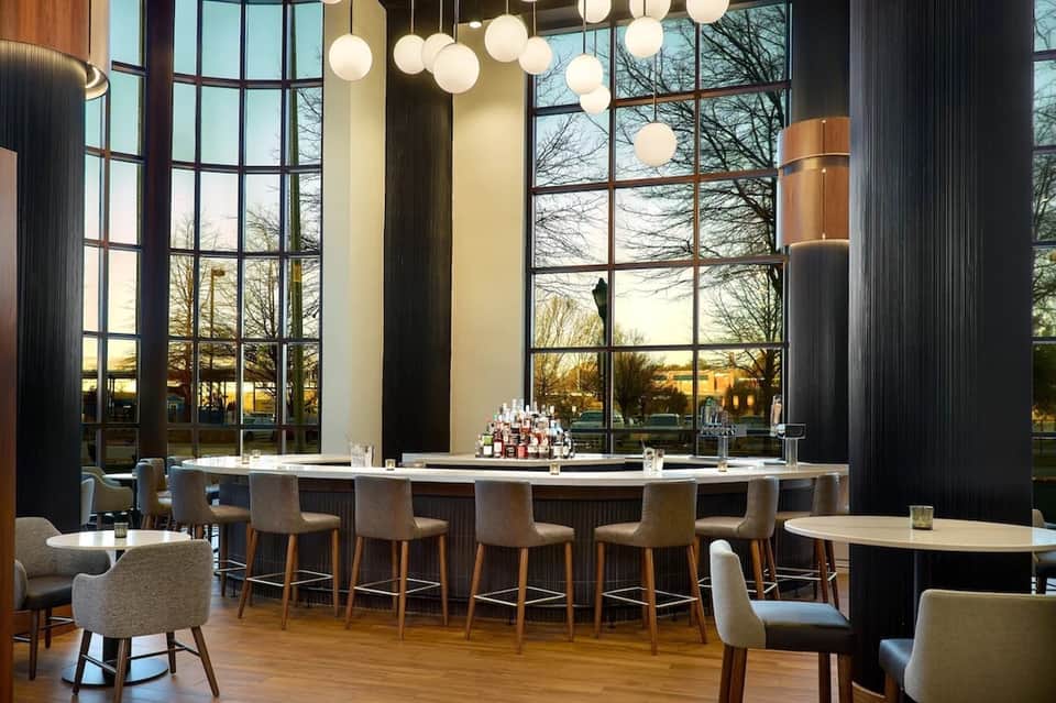 Contemporary hotel bar with floor-to-ceiling windows at sunset, hanging sphere lighting, and modern bar seating