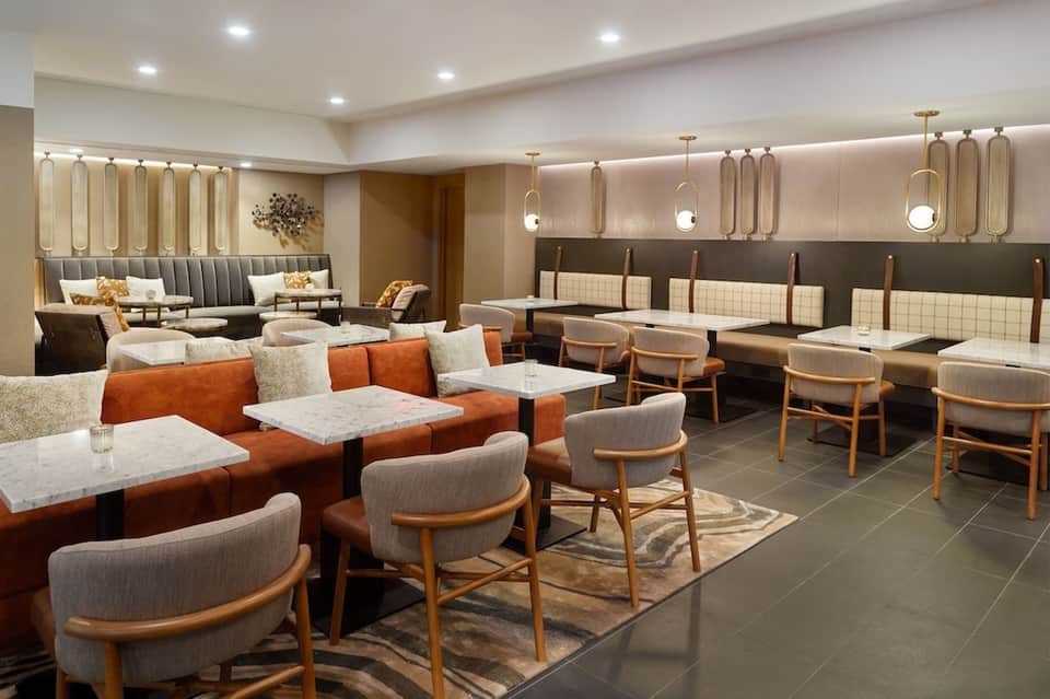 Contemporary hotel lounge with orange and gray seating, pendant lighting, and modern design elements