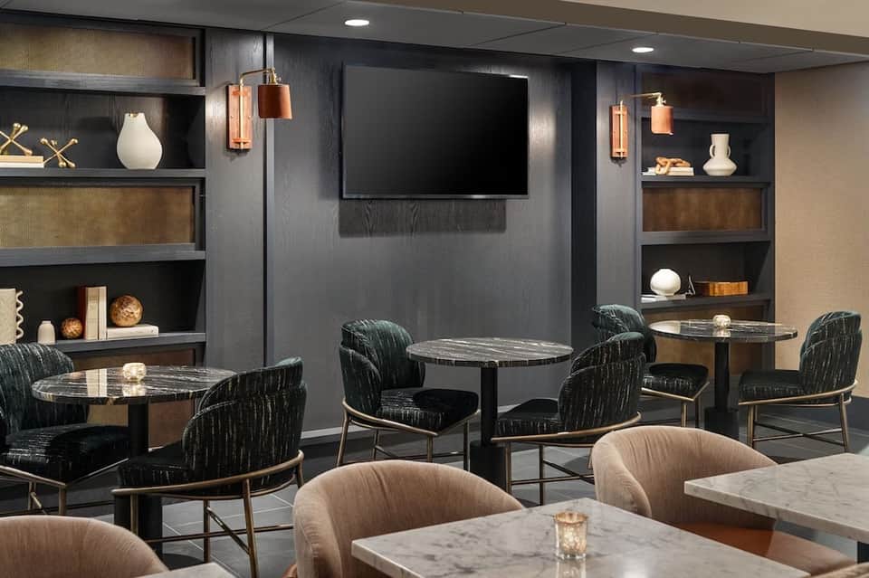 Contemporary lounge space with marble tables, patterned chairs, TV, and built-in shelving