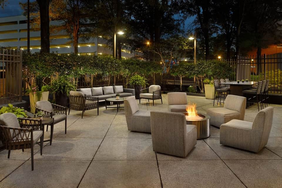 Evening courtyard with fire pit, neutral lounge seating, greenery, and ambient lighting