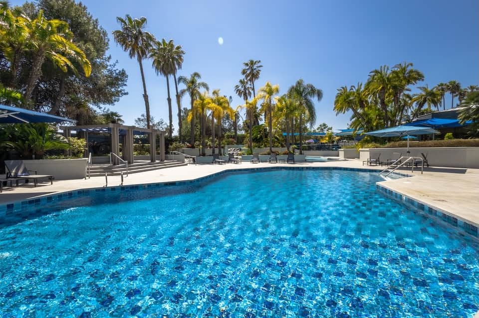Resort pool with palm trees, blue umbrellas, and modern architectural elements