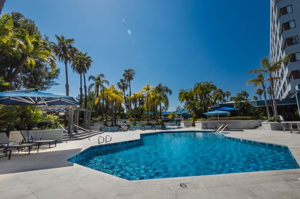 Curved resort pool with palm trees and blue umbrellas under clear sky