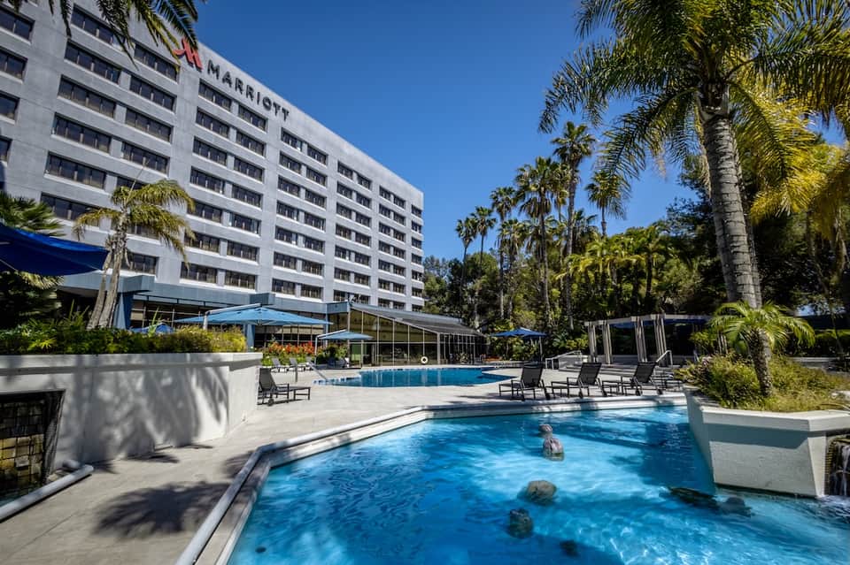 Marriott hotel with dual pools, loungers, and palm trees in front of multi-story white building