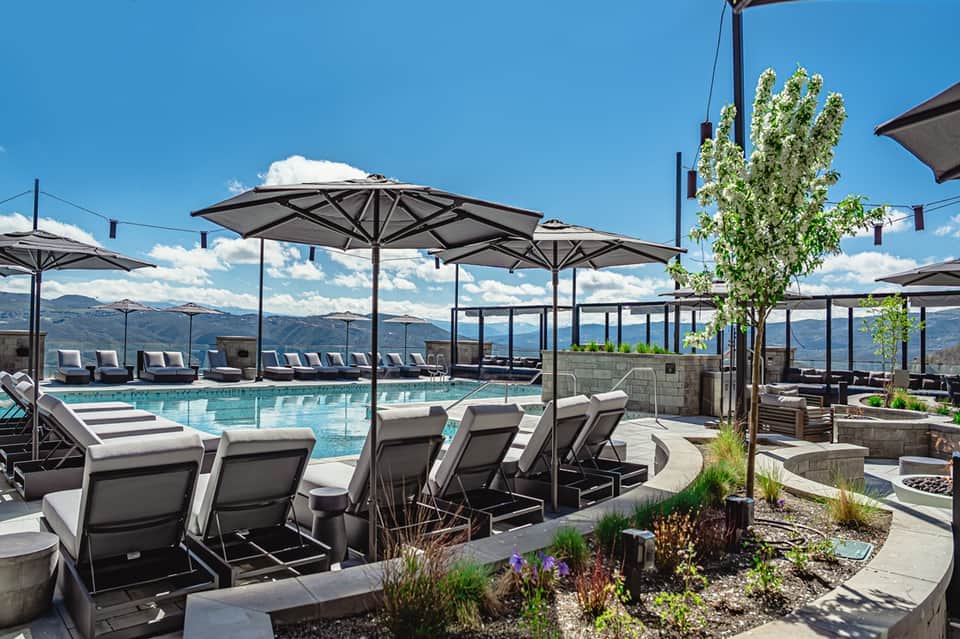 Resort pool deck with mountain views, lounge chairs, black umbrellas, and landscape design