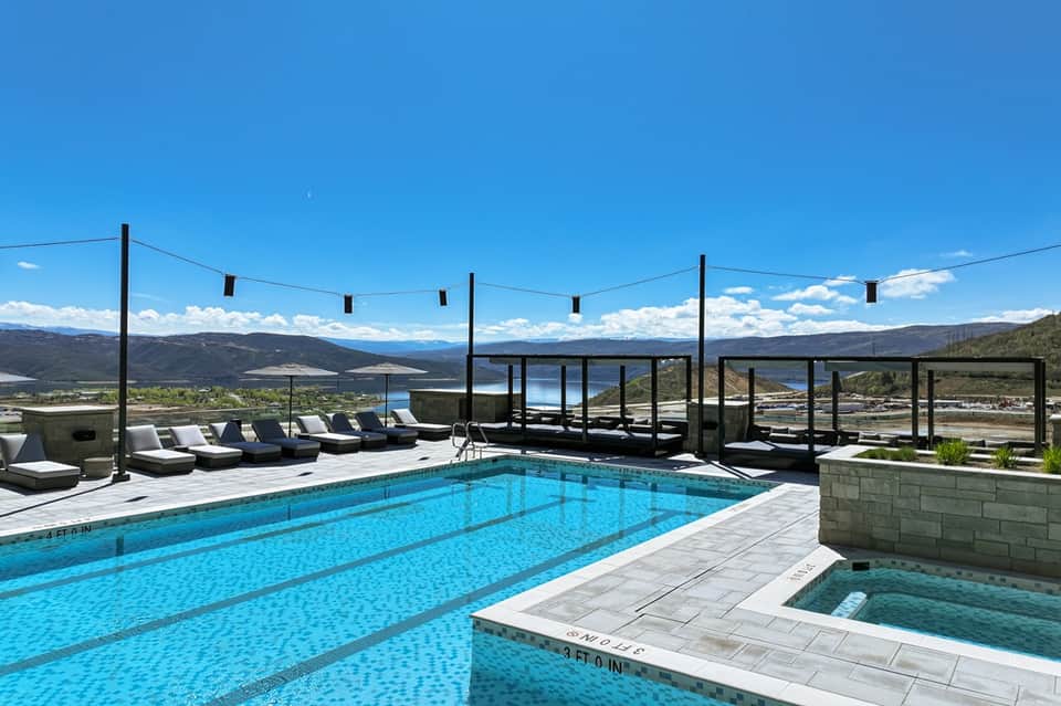 Modern infinity pool with mountain views, lounge chairs, and spa hot tub at sunset