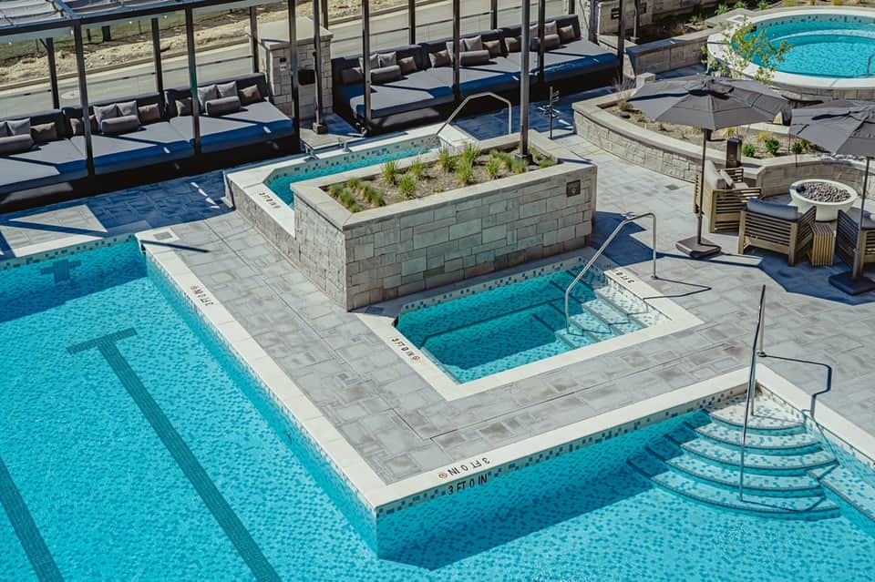 Luxury resort pool deck with multiple pools, cabanas, loungers, and fire pit surrounded by landscaping