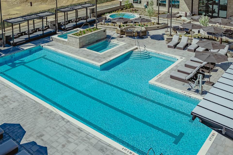 Resort pool complex with lap lane, hot tub, lounge chairs, umbrellas, and mountain views