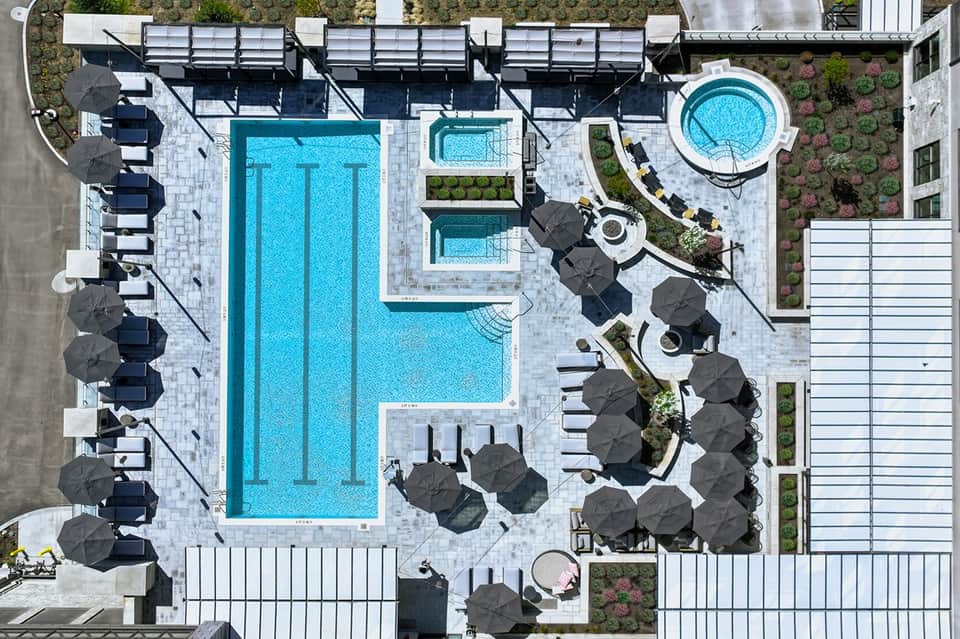 Overhead view of modern rooftop pool deck with rectangular lap pool, lounge chairs, and umbrellas