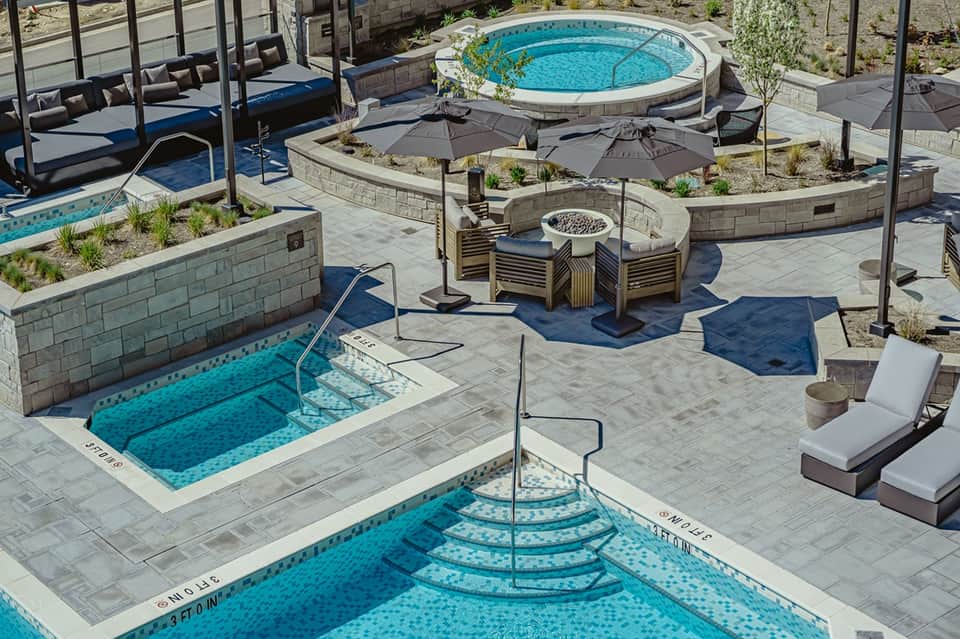 Outdoor resort pool deck with multiple pools, fire pit, lounge seating, and landscaping