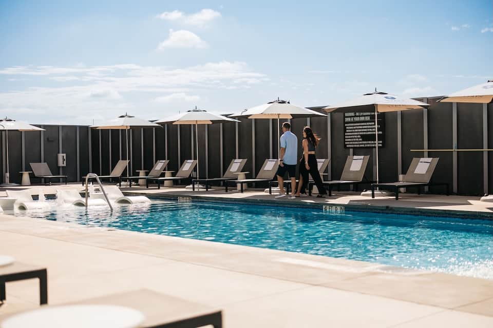 Outdoor pool with tan umbrellas, lounge chairs, and dark privacy partitions