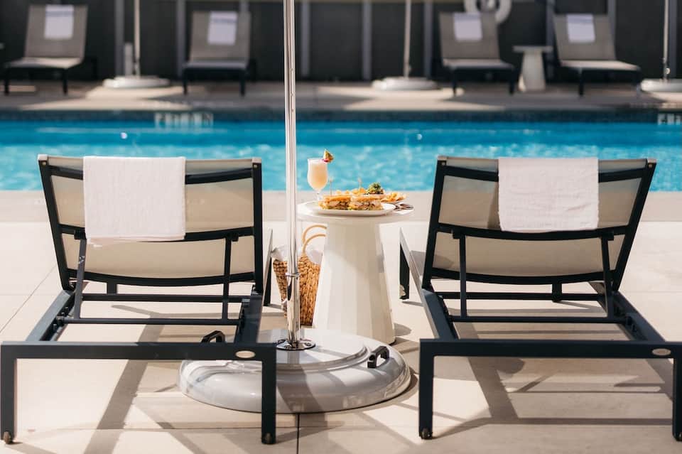 Two lounge chairs by resort pool with umbrella, food, and beverage service setup