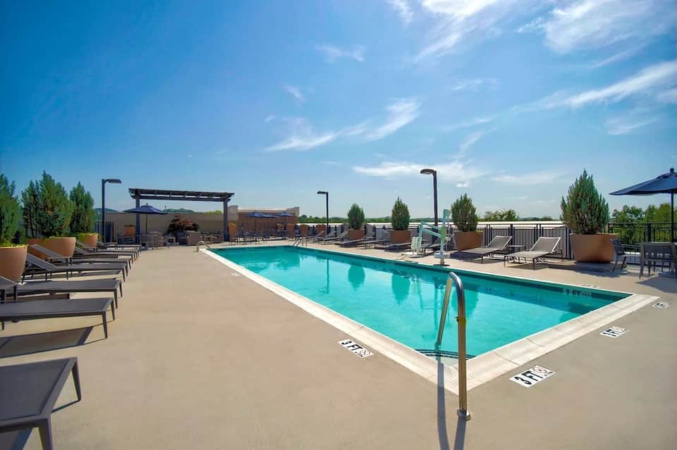Rooftop pool with city skyline, lounge chairs, pergola, and blue umbrellas at daytime