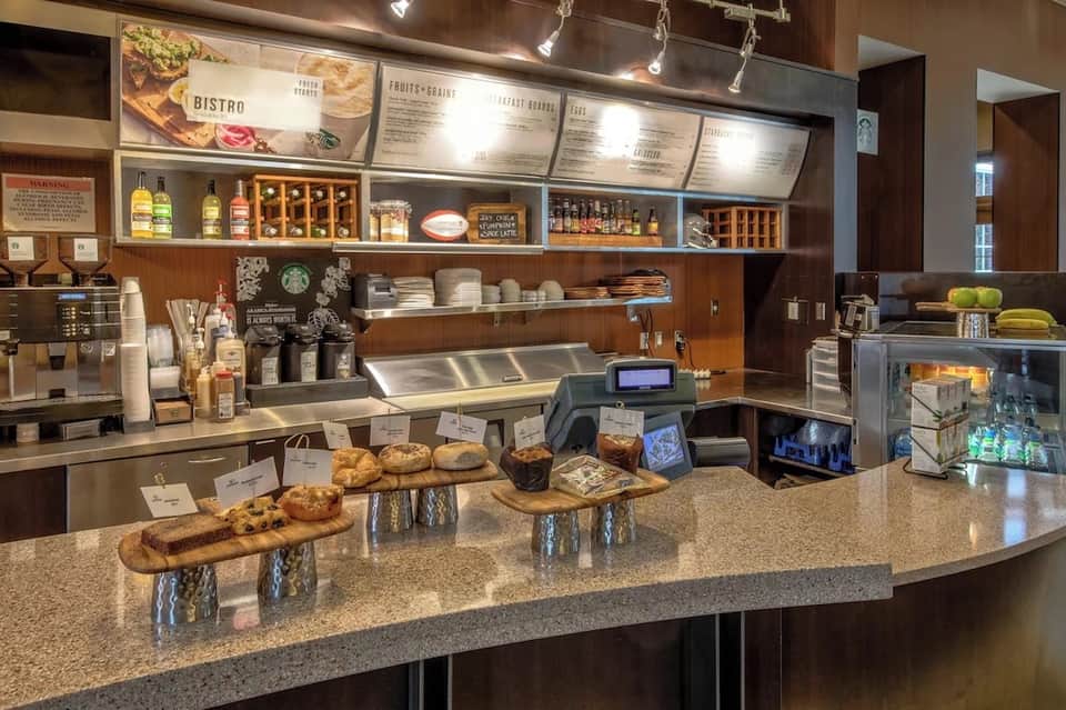 Starbucks cafe counter with menu boards, pastries, beverages, and espresso machine in bright setting