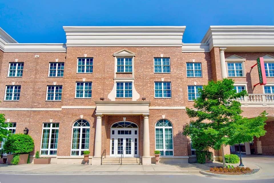 Historic red brick building facade with classical columns, blue windows, and manicured landscaping