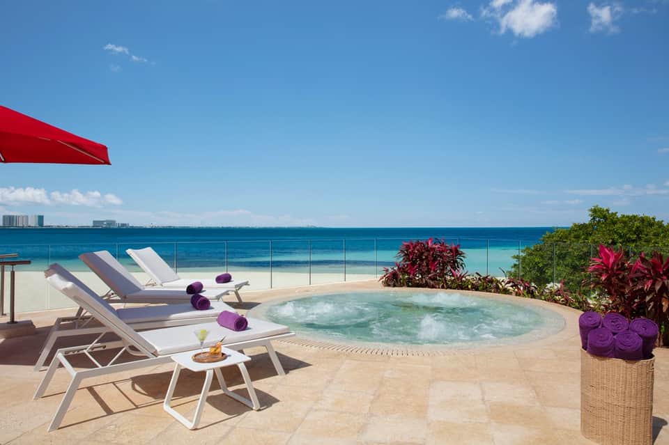 Beachfront spa area with lounge chairs, hot tub, ocean view, and tropical flowers