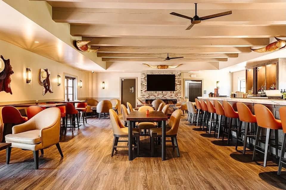 Spacious lounge with wooden ceiling beams, orange and white seating, bar, and fireplace
