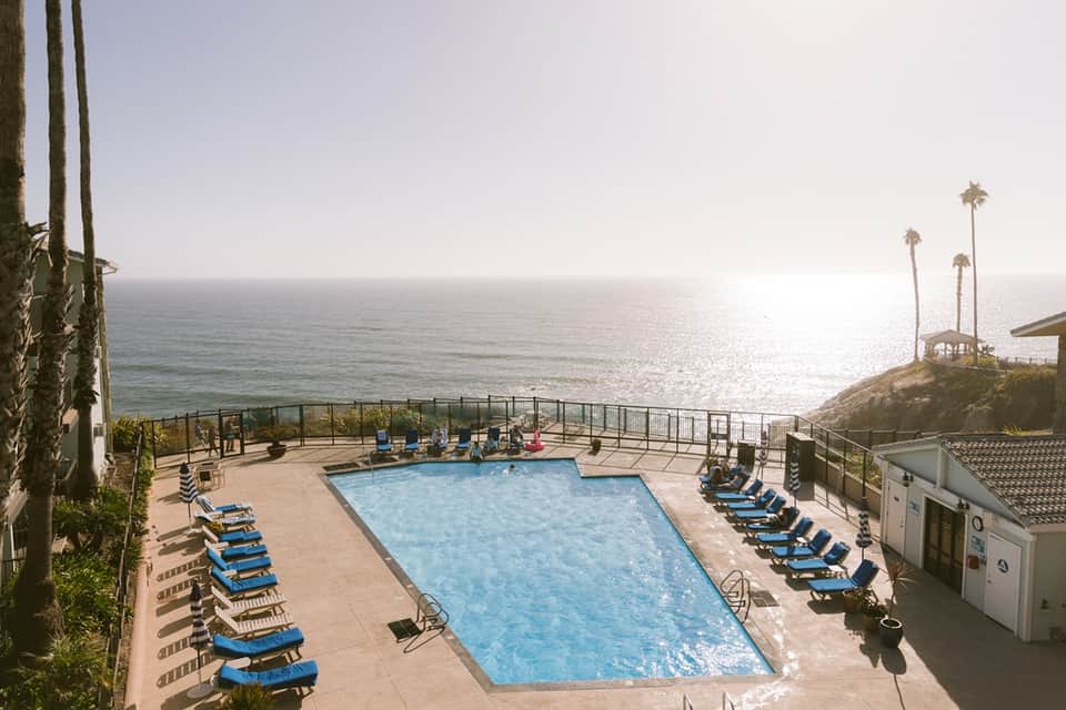 Resort pool deck with blue loungers, palm trees, and sparkling ocean horizon at sunset