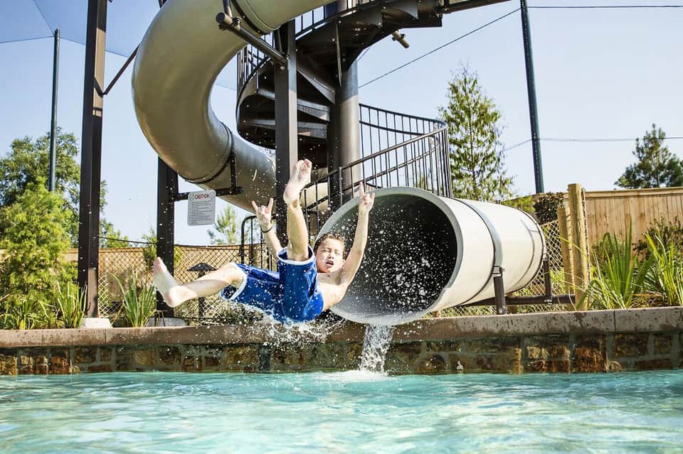 Child splashing down water slide into pool at recreational water park facility