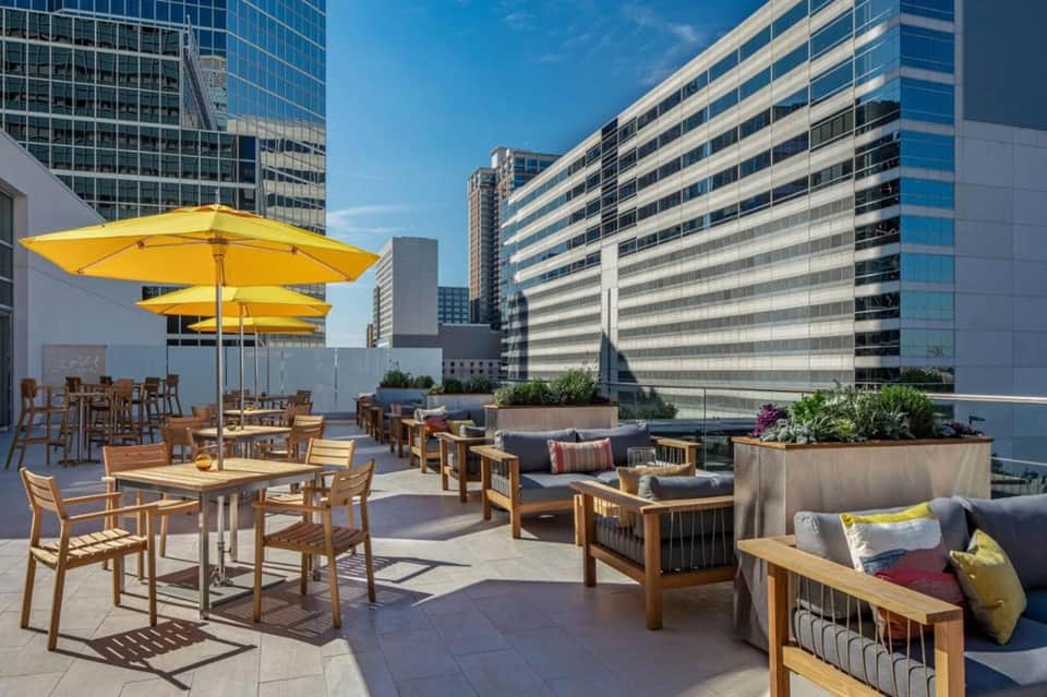 Rooftop lounge with yellow umbrellas, modern seating, city skyline views, and daybed pods