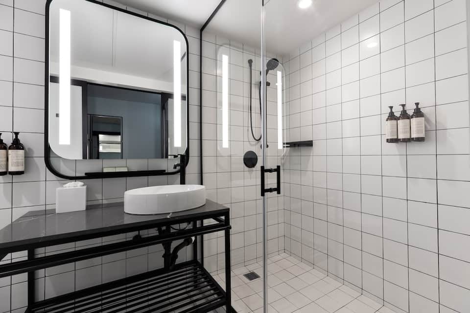 Contemporary bathroom with white subway tiles, black vanity, and illuminated mirror