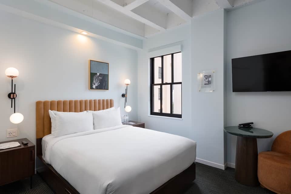 Modern hotel bedroom with tan headboard, white bedding, and minimalist décor