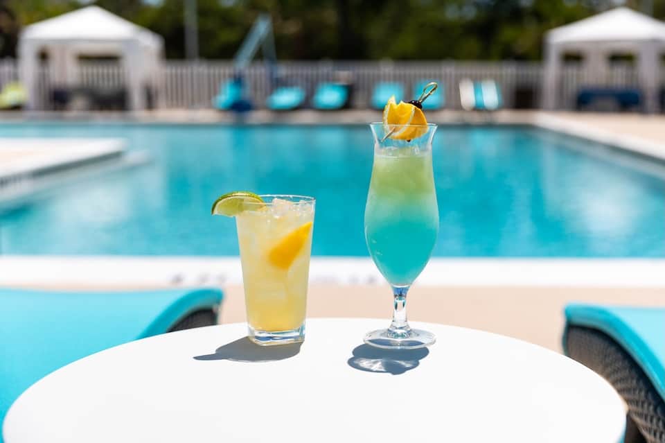 Poolside cocktails on white table with blue lounge chairs and resort pool in background