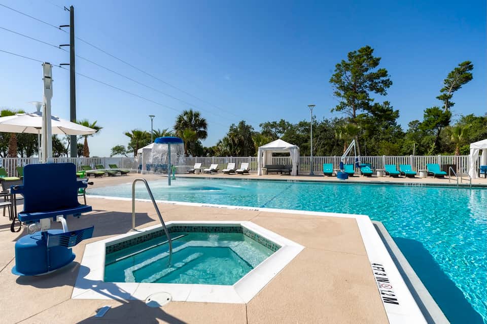 Resort pool area with hot tub, palm trees, white umbrellas, and clear blue water