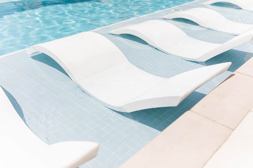 Swimming pool with white lounge chairs partially submerged in clear blue water