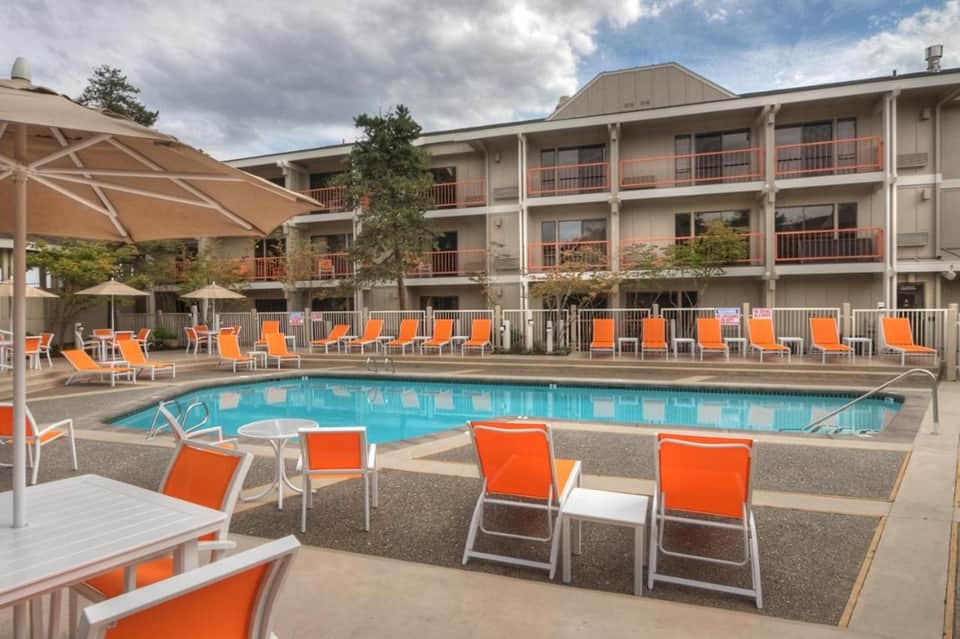 Resort pool with orange lounge chairs, white umbrellas, and multi-story building backdrop