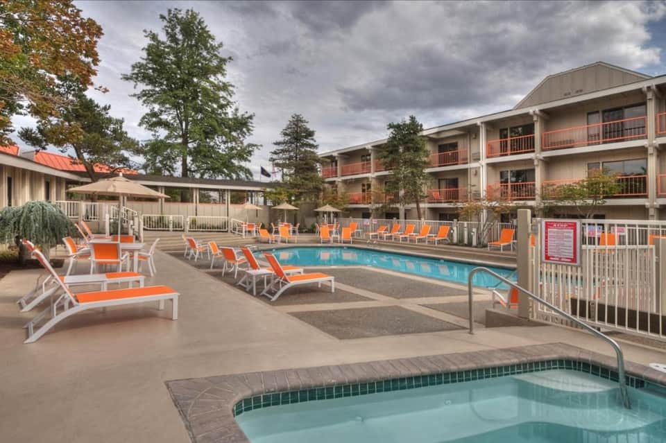Resort pool deck with orange lounge chairs, multi-story building, and spa area with umbrellas