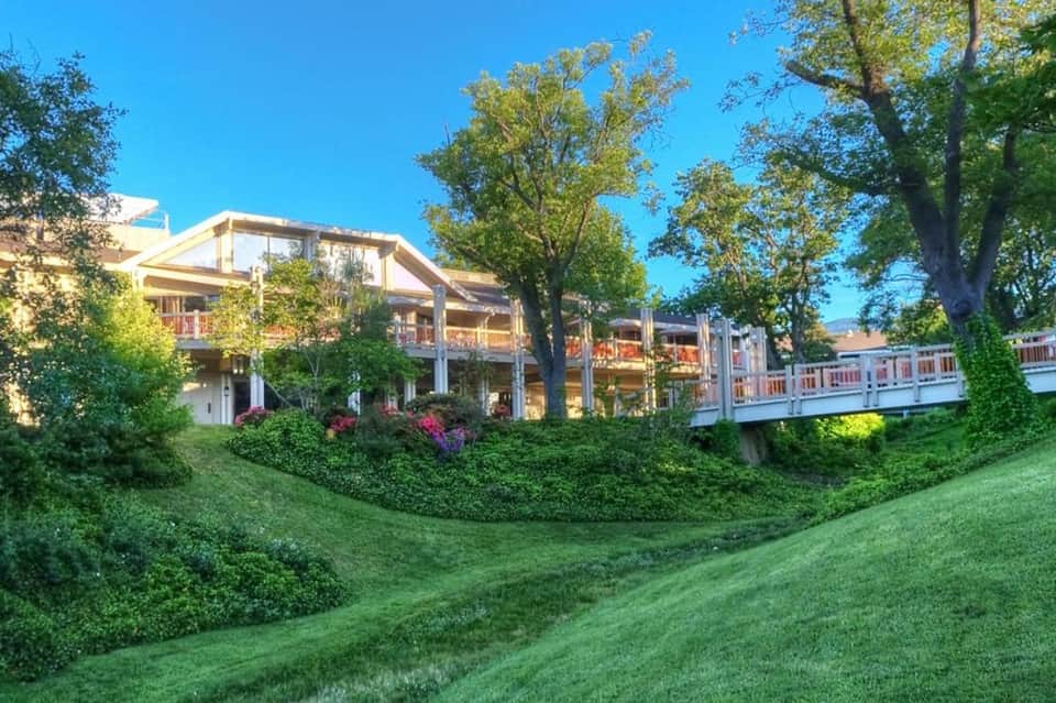 Resort outdoor gathering space with modern lodge building, white railings, trees, and manicured lawn