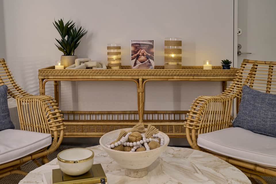 Elegant spa waiting area with rattan chairs, marble table, decorative bowl, and gold-trimmed console