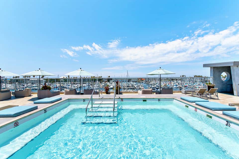 Rooftop swimming pool with marina views and white umbrellas on sunny day