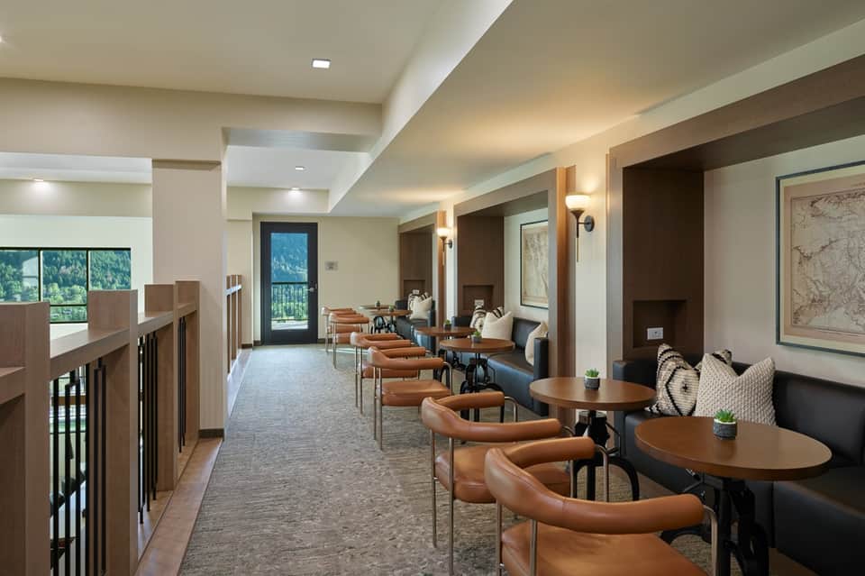 Hotel corridor with leather seating, round tables, wood accents, and mountain view balcony