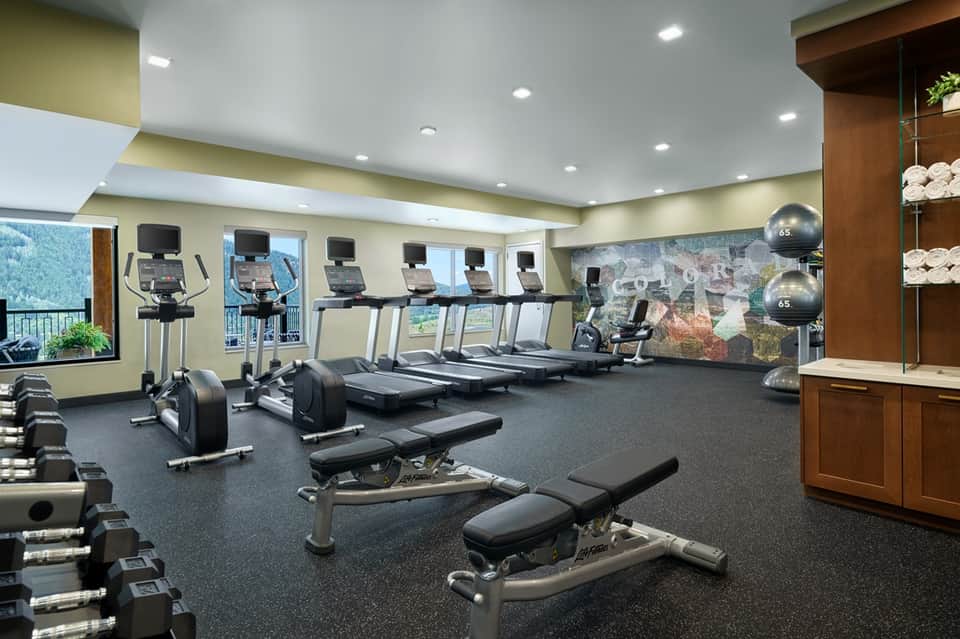 Modern fitness center with treadmills, stationary bikes, dumbbells, and large windows with mountain views