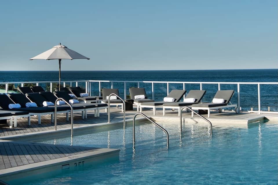 Rooftop pool deck with lounge chairs, umbrella, and ocean horizon view
