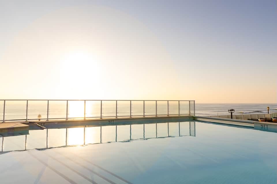 Oceanfront infinity pool reflecting sunset sky with metal railing and sea view