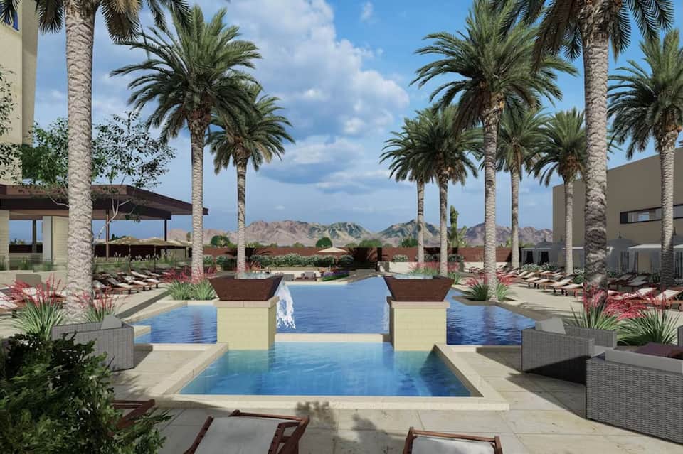 Desert resort pool with palm-lined architecture, mountain views, lounge chairs, and modern buildings.