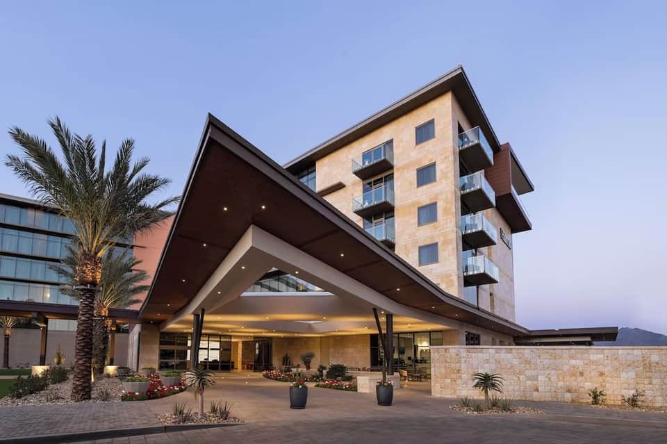 Modern hotel exterior at dusk with contemporary architecture, palm trees, and illuminated entrance portico