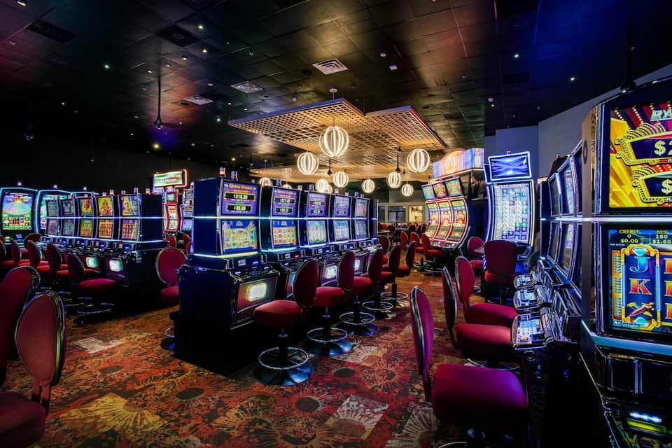 Casino floor with slot machines and red chairs under decorative pendant lights