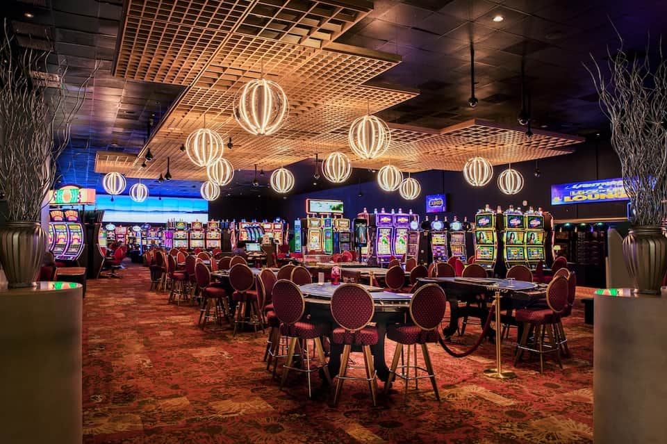 Casino floor with slot machines, neon sphere lighting, gaming tables, and vibrant decor