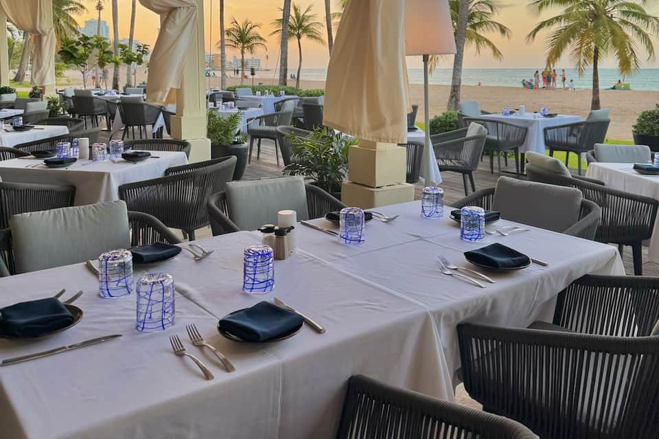 Elegant beachfront dining area with white tablecloths, dark chairs, and ocean view
