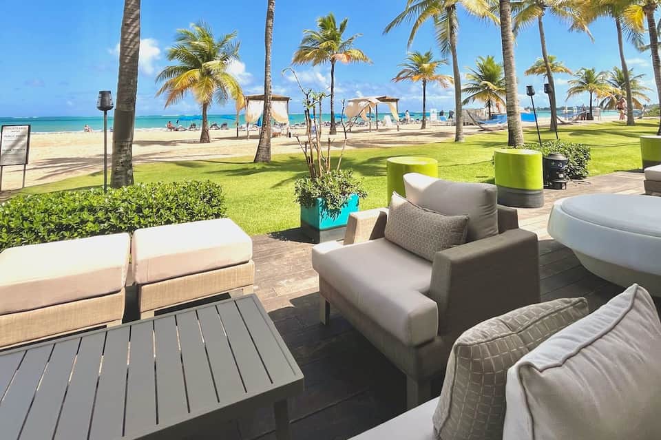 Beachfront resort patio with comfortable seating, palm trees, and ocean view