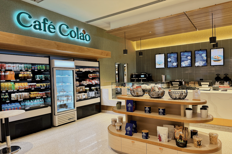 Café Colão interior with neon sign, beverage coolers, counter seating, and menu displays