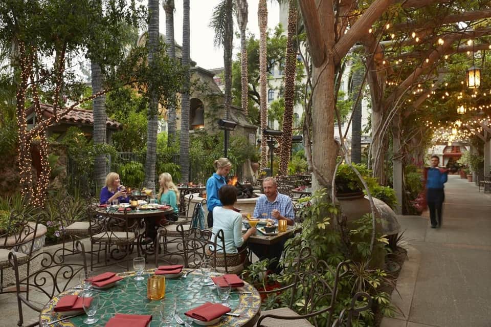Outdoor courtyard dining area with ivy-covered trees, string lights, and guests dining