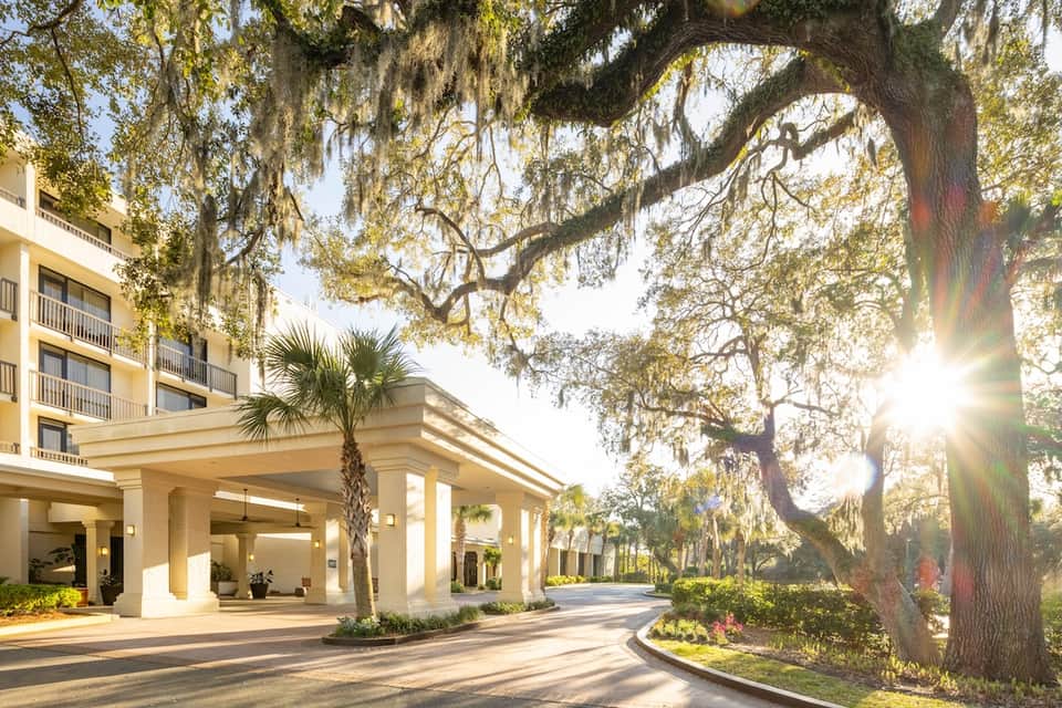 Hotel entrance with grand columns, yellow facade, and large oak trees with Spanish moss
