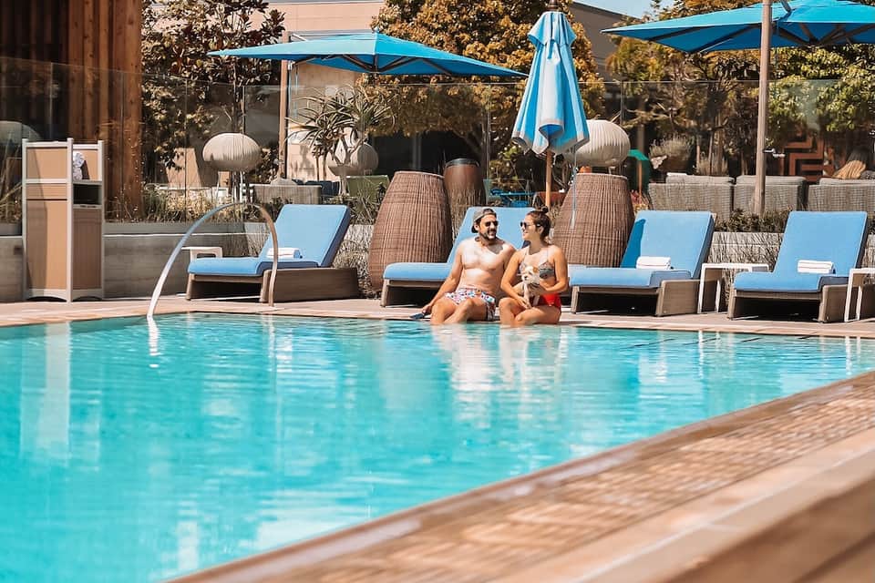 Resort pool area with blue umbrellas, lounge chairs, and two guests relaxing poolside