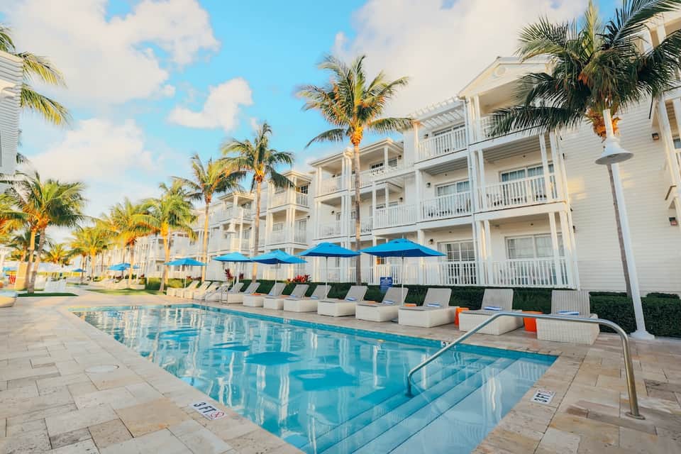 Residential resort pool with blue umbrellas, white buildings, and palm trees lining grounds