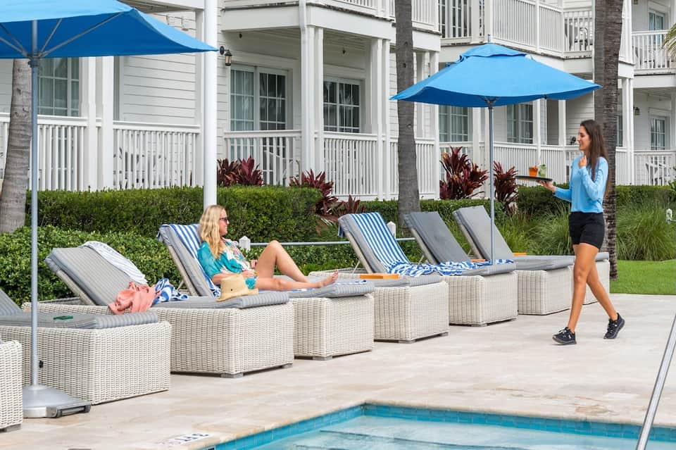 Resort poolside with lounge chairs, blue umbrellas, and palm trees at vacation property