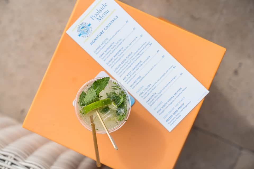 Poolside cocktail with mint and lime on orange napkin next to signature cocktail menu